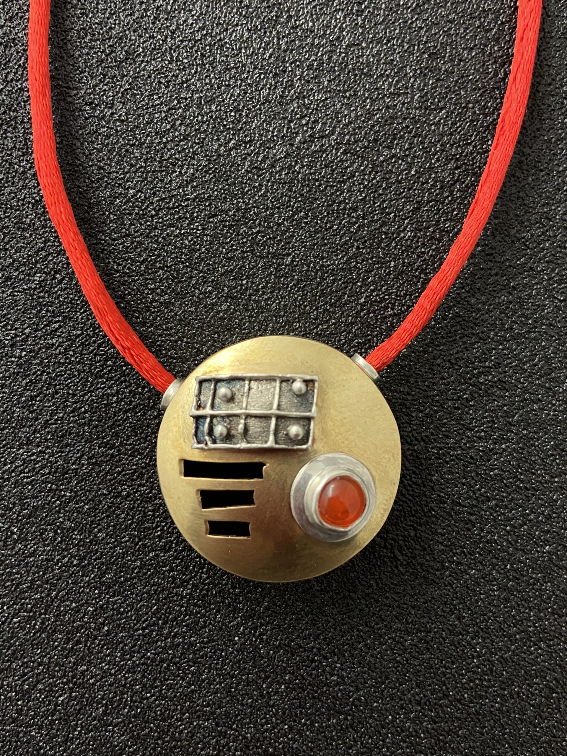 photo of a round hollow form pendant on a red cord